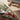 A flat lay of a dried flower bouquet arrangement including celosia, aveena, phalaris, and long grasses with a linen ribbon. The bouquet is laid out on a wooden surface with a blurred background featuring a book and decorative tassels.